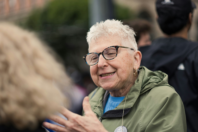 An elder woman at a community meeting gestures and speaks emphatically