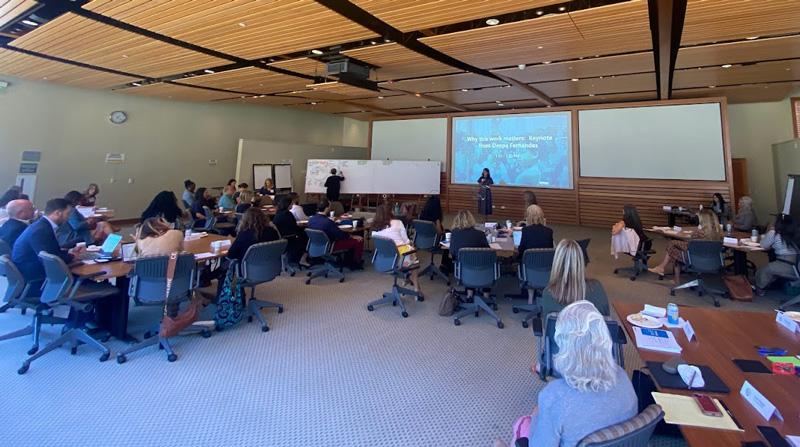 A wider view of the conference room showing attendees and speaker at the All In For Kids round table meeting