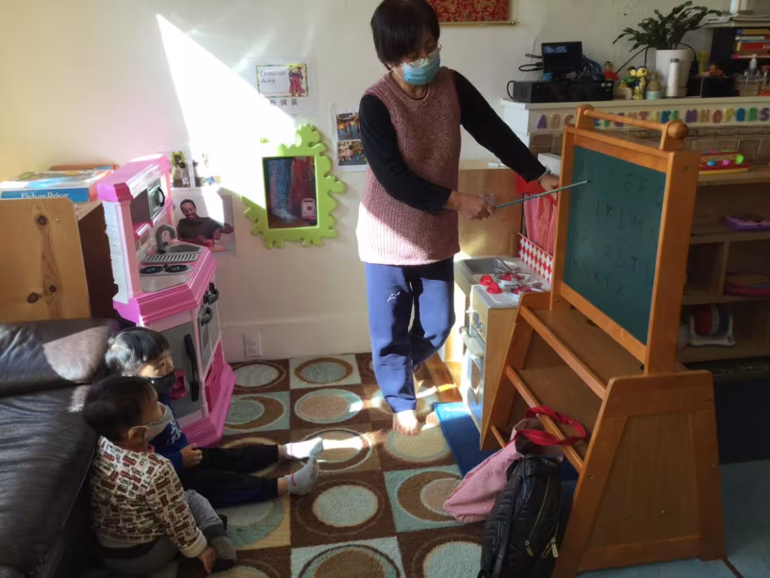 Two kids watching a woman pointing at a chalkboard
