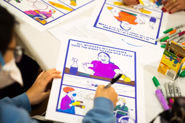 Domestic workers creating posters to raise awareness for paid sick leave. Image shows people coloring in posters.